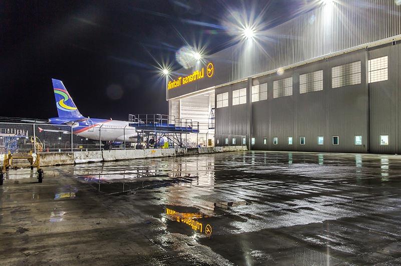 汉莎航空技术公司重型维修设施外的夜晚. Airplane entering hangar in the back.